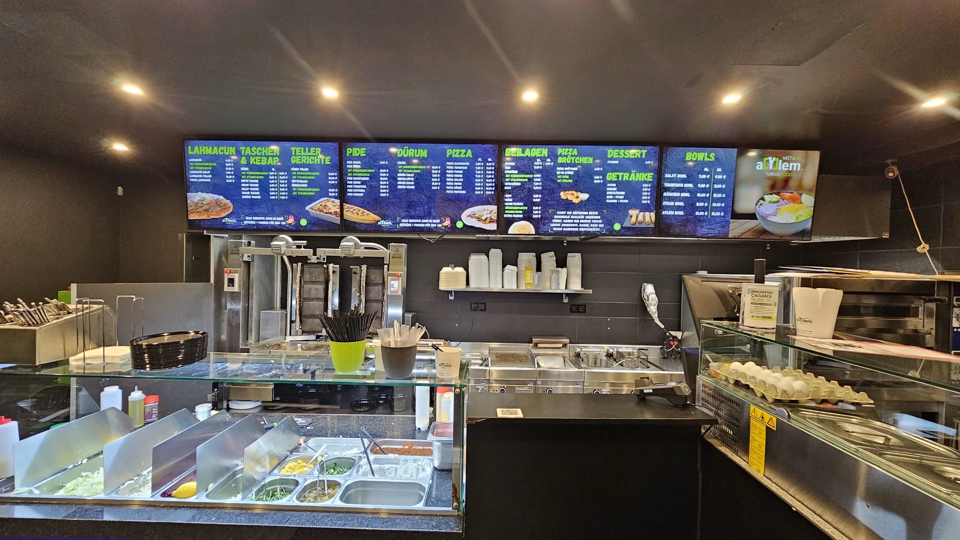 Gastraum von Aylem Eat & Meet in Hamm mit der komplett bespielten Menüboard-Wand über der Theke