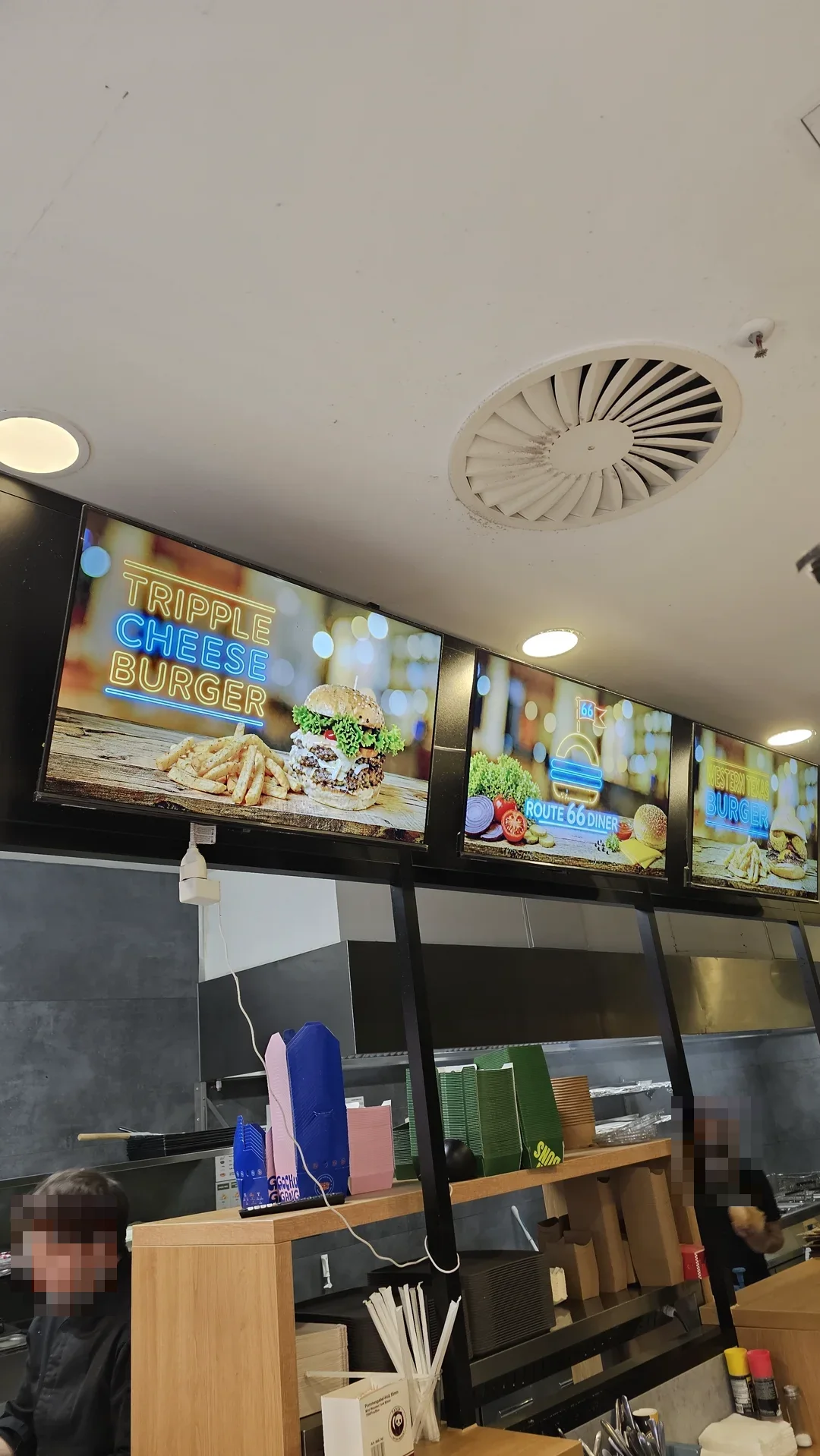 Drei digitale Menüboards des Route 66 Diner im Neon-Look über der offenen Küche